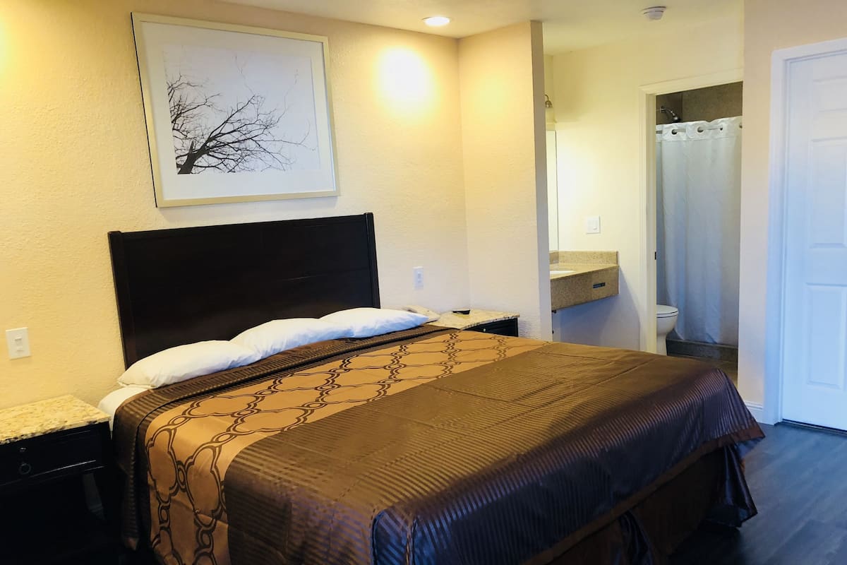 A neatly made bed with a patterned bedspread and pillows, a bedside table with a lamp, and a framed picture on the wall.