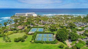 Um resort com várias quadras de tênis, um edifício grande e vista para o oceano.
