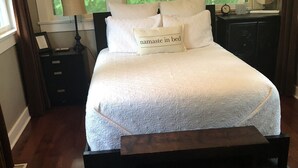 Un lit bien fait, avec un oreiller orné de l’inscription « namasté au lit », une table de chevet avec une lampe, une horloge et un cadre contenant une photo.