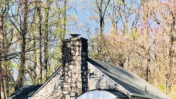 Un bâtiment en pierre doté d’un porche et d’une pancarte « Bienvenue », entouré d’arbres et d’une clôture.