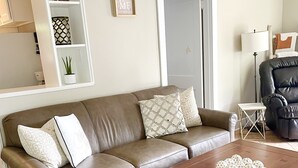 Un salon avec un canapé en cuir marron, des coussins à motifs, une table basse en bois agrémentée d’objets décoratifs, une petite table d’appoint blanche et une plante en pot.