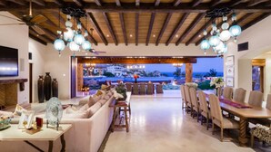 Amplia sala de estar con un sofá grande, mesa de comedor y sillas, que conduce a una terraza exterior con piscina y vista al océano.