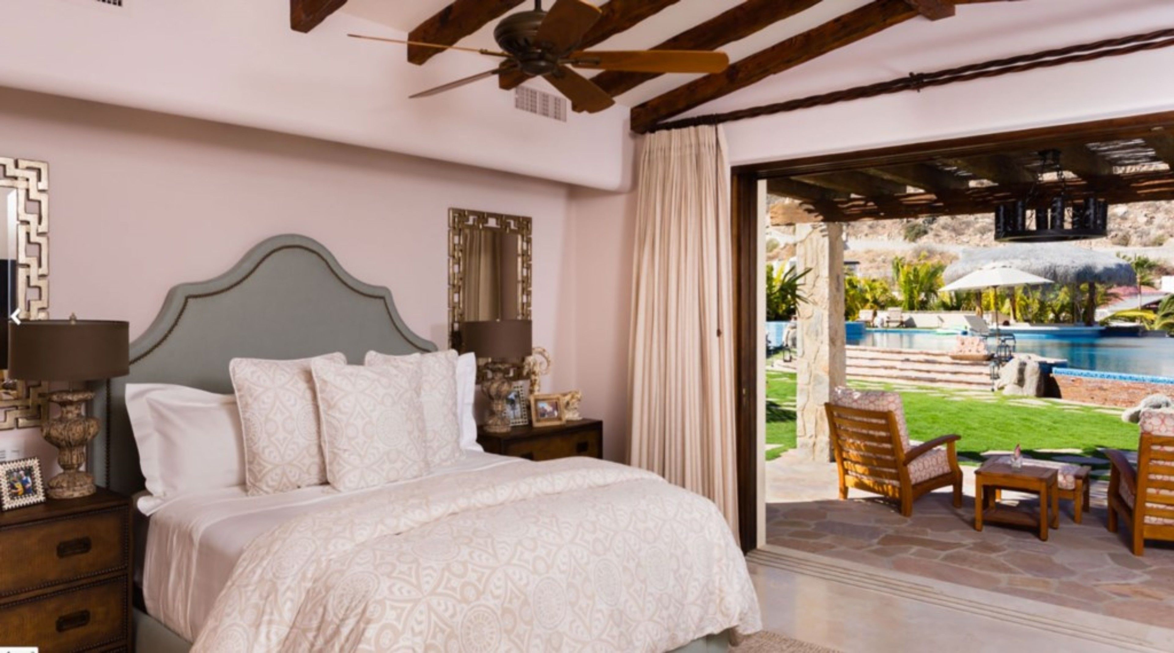 A bedroom with a bed, nightstands, a ceiling fan, and a view of an outdoor pool area.