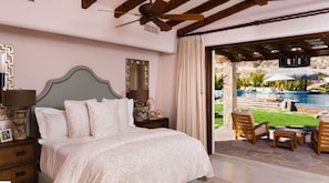 A bedroom with a bed, nightstands, a ceiling fan, and a view of an outdoor pool area. - Casa de Karma by Cabo Platinum (Cabo San Lucas)