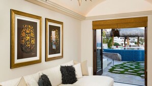 Una habitación con sofá blanco, dos obras de arte enmarcadas y vistas a una piscina y zona exterior.