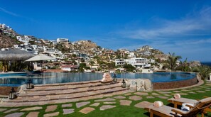 A resort pool with a stone deck, lounge chairs, and a view of hillside buildings. - Casa de Karma by Cabo Platinum (Cabo San Lucas)