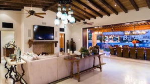 Una sala de estar moderna con un televisor grande, asientos cómodos, jarrones decorativos y vistas a una zona de piscina.