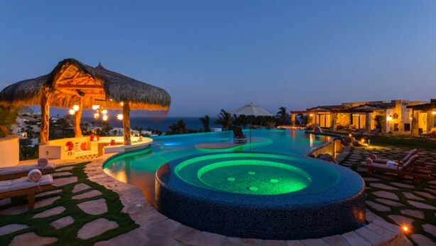 Piscina de resort con un jacuzzi circular, sillas de descanso y una sombrilla de paja.