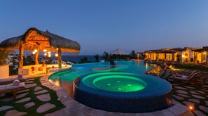 Une piscine de villégiature avec un jacuzzi circulaire, des chaises longues et un parasol en chaume.