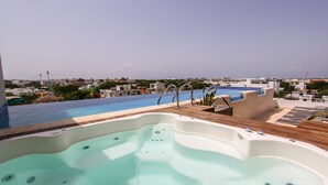 Een dakterras met een uitgestrekt zwembad, een jacuzzi en ligbedden, met uitzicht op een stadsgezicht.
