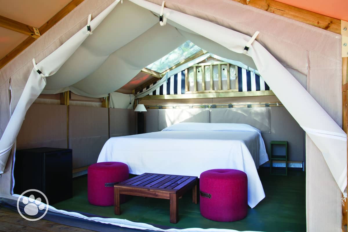 Een tentverblijf met een bed, een tafel en twee krukken.