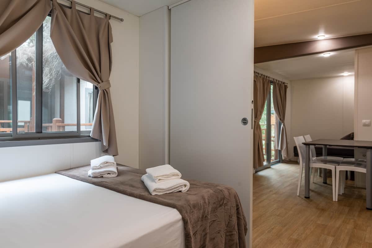 Een slaapkamer met een bed, een raam met gordijnen, een badkamedeur en een eethoek met stoelen en een tafel.