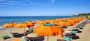 A beach with rows of orange umbrellas and green lounge chairs.