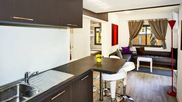A modern kitchen with a central island, a dining area with a sofa and chairs, and a living space with a red floor lamp.