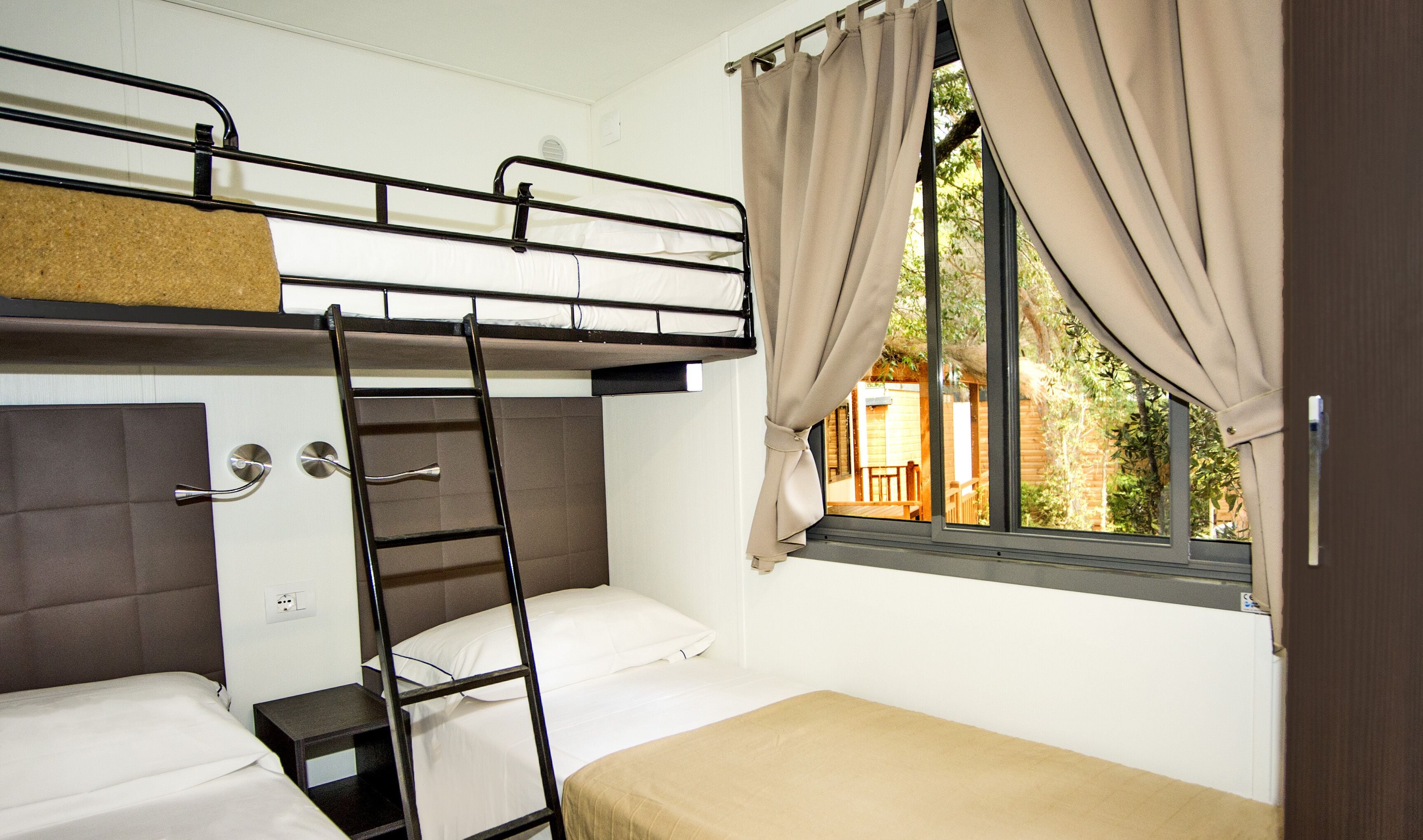 A bunk bed room with a ladder, a window with curtains, and a view of the outside.