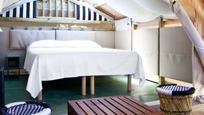 Eine Zelthotelunterkunft mit einem Bett, einem Holztisch und zwei Korbstühlen.