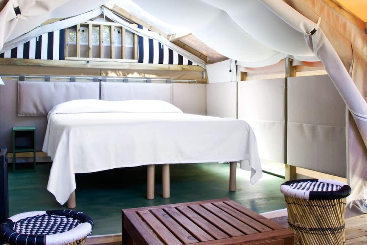 Een tentaccomodatie met een bed, een houten tafel en twee rieten stoelen.