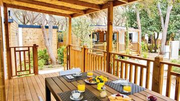 Una terraza de madera con el desayuno servido, incluyendo platos, vasos y un bol de frutas.