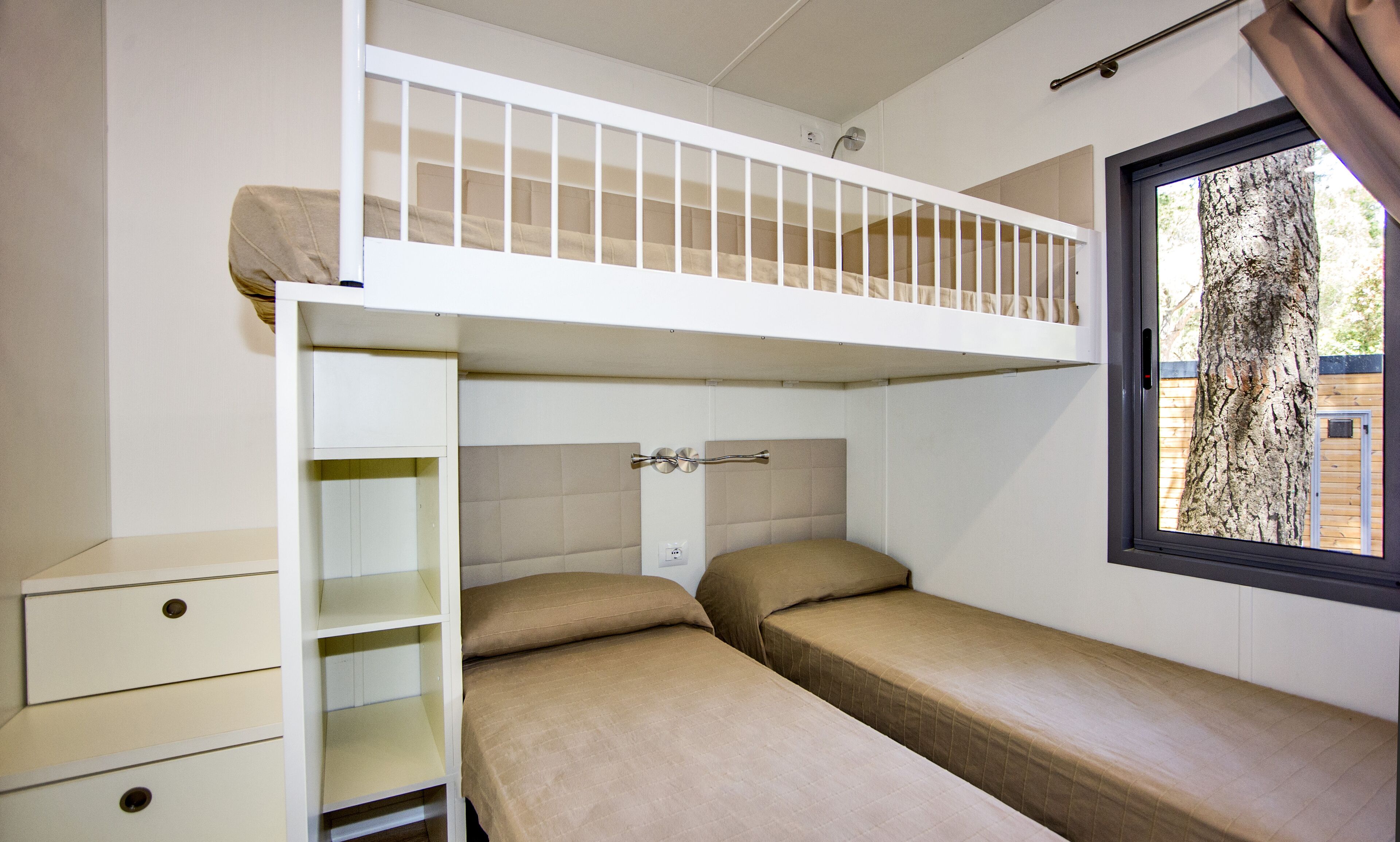 A bunk bed room with a window, a white dresser, and a view of a tree outside.