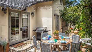An outdoor patio with a round table set for dining, surrounded by wicker chairs, a barbecue grill, and string lights. - 3770 Stone's Throw ~ Walk to the Ocean and Town (Carmel)