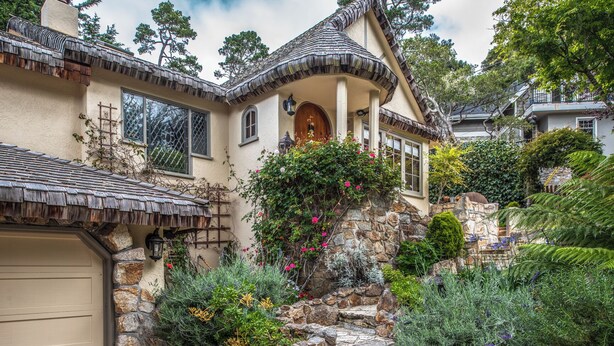 A house with a stone facade, a wooden porch, and a garden with various plants and flowers. - 3770 Stone's Throw ~ Walk to the Ocean and Town (Carmel)