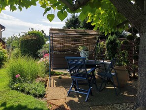 Eine Garten-Terrasse mit Holztisch und -stühlen, umgeben von üppiger Bepflanzung und einem Holzzaun.