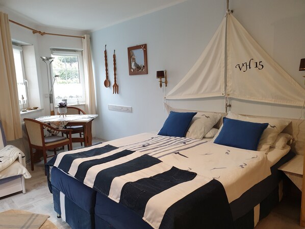 Ein Schlafzimmer mit einem Bett, einem Nachttisch, einem Sessel, einem Fenster und einer Wandleuchte.