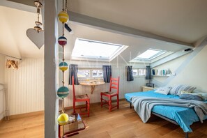 A bedroom with a skylight, a bed with blue bedding, a red chair, and a small table with a lamp.