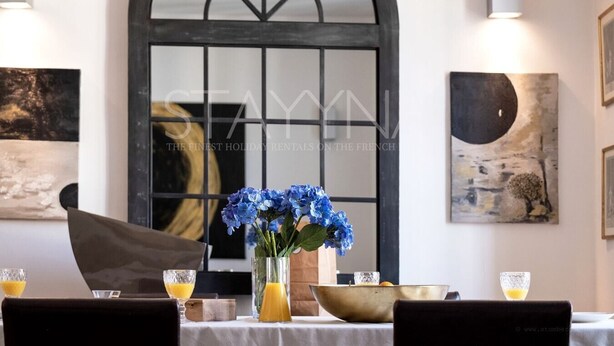 A dining table with a vase of blue flowers, a glass of orange juice, and a candle holder. - Chez Aynur 2 bedroom apartment VRBO (Nice)