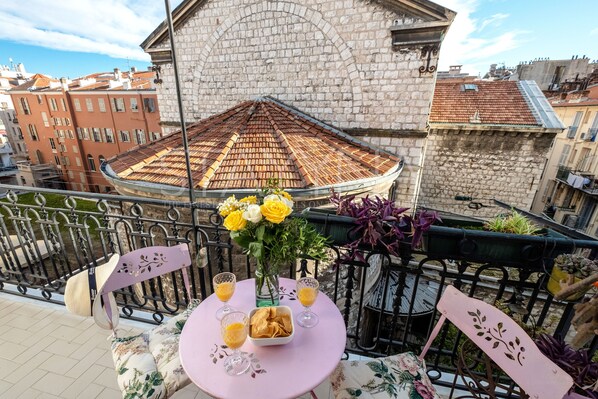 A balcony with a table set for two, featuring a vase with flowers and glasses of a beverage.