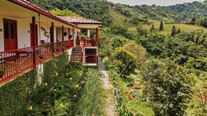 A building with a red balcony, surrounded by lush greenery and a hillside view. - Lodge Paraiso Verde Manizales (Manizales)