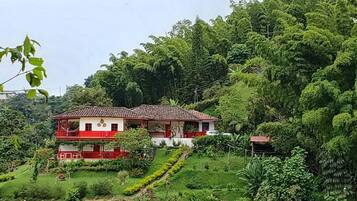 A two-story house with a red and white exterior, surrounded by lush greenery and trees.