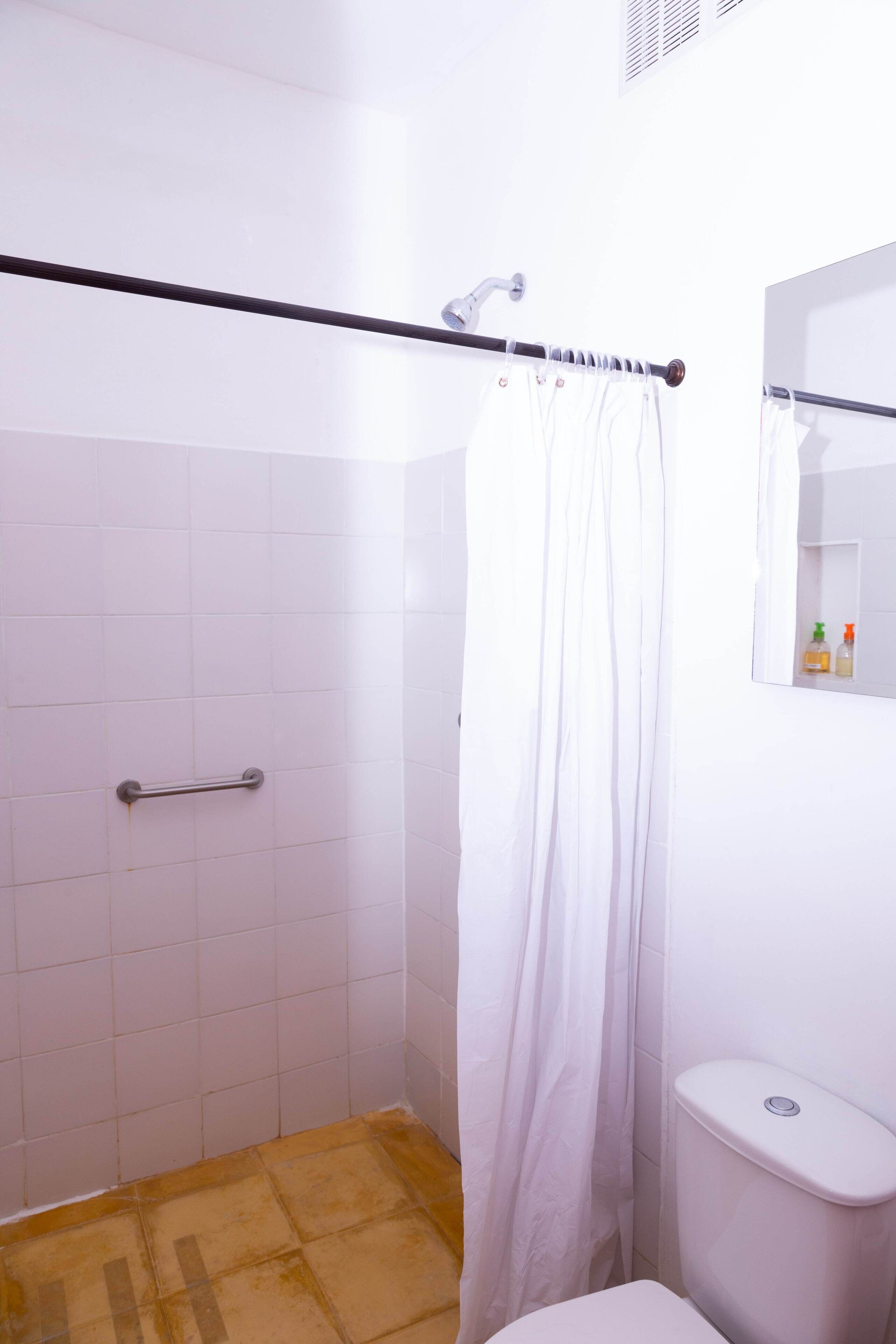 Een badkamer met douche, toilet en een handgreep.