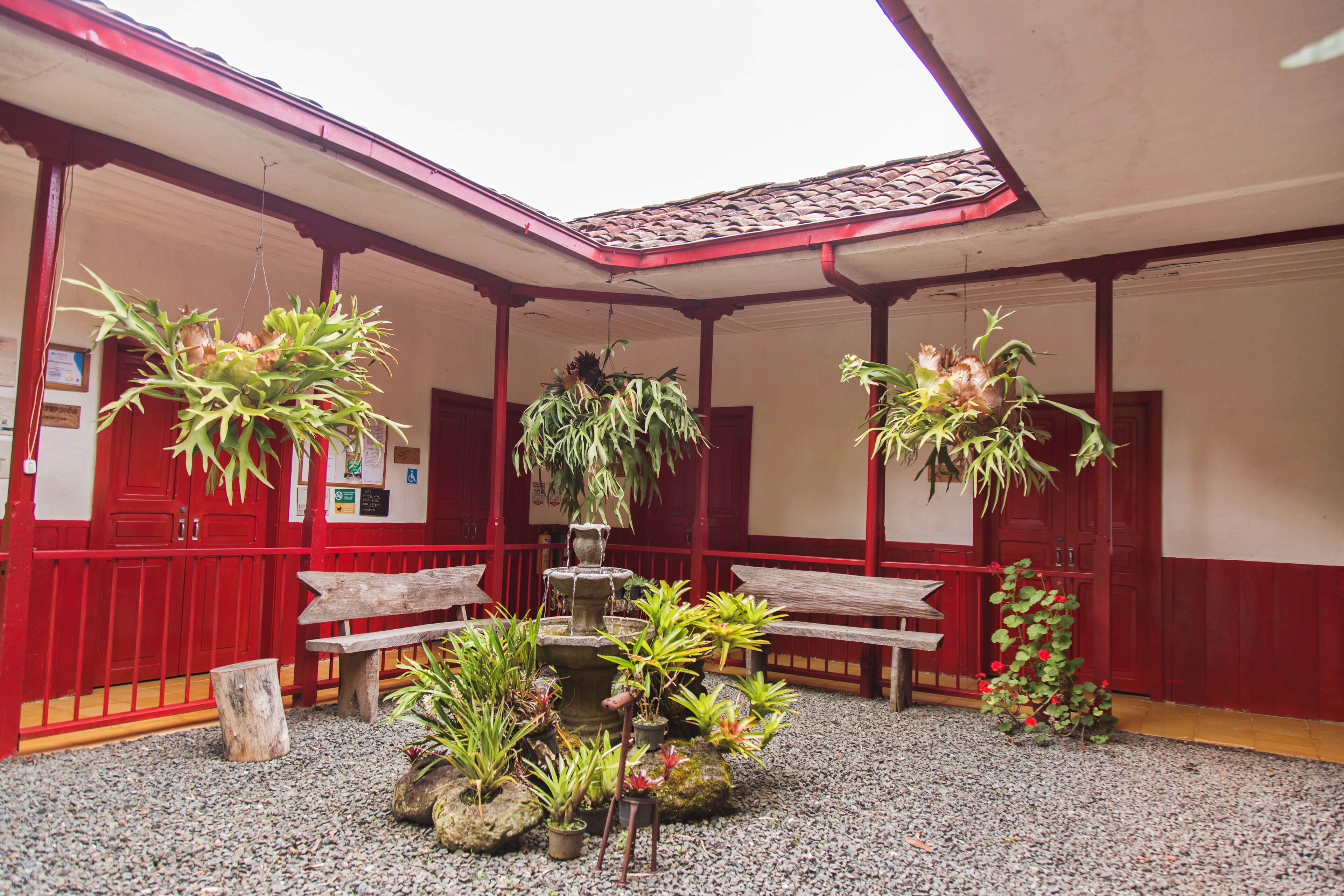 Une cour avec des murs rouges, une fontaine et diverses plantes en pot.