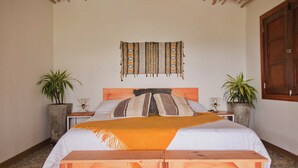 A bedroom with a wooden headboard, a bed with white bedding and a yellow throw, two bedside tables with lamps, and two potted plants. - Lodge Paraiso Verde Manizales (Manizales)