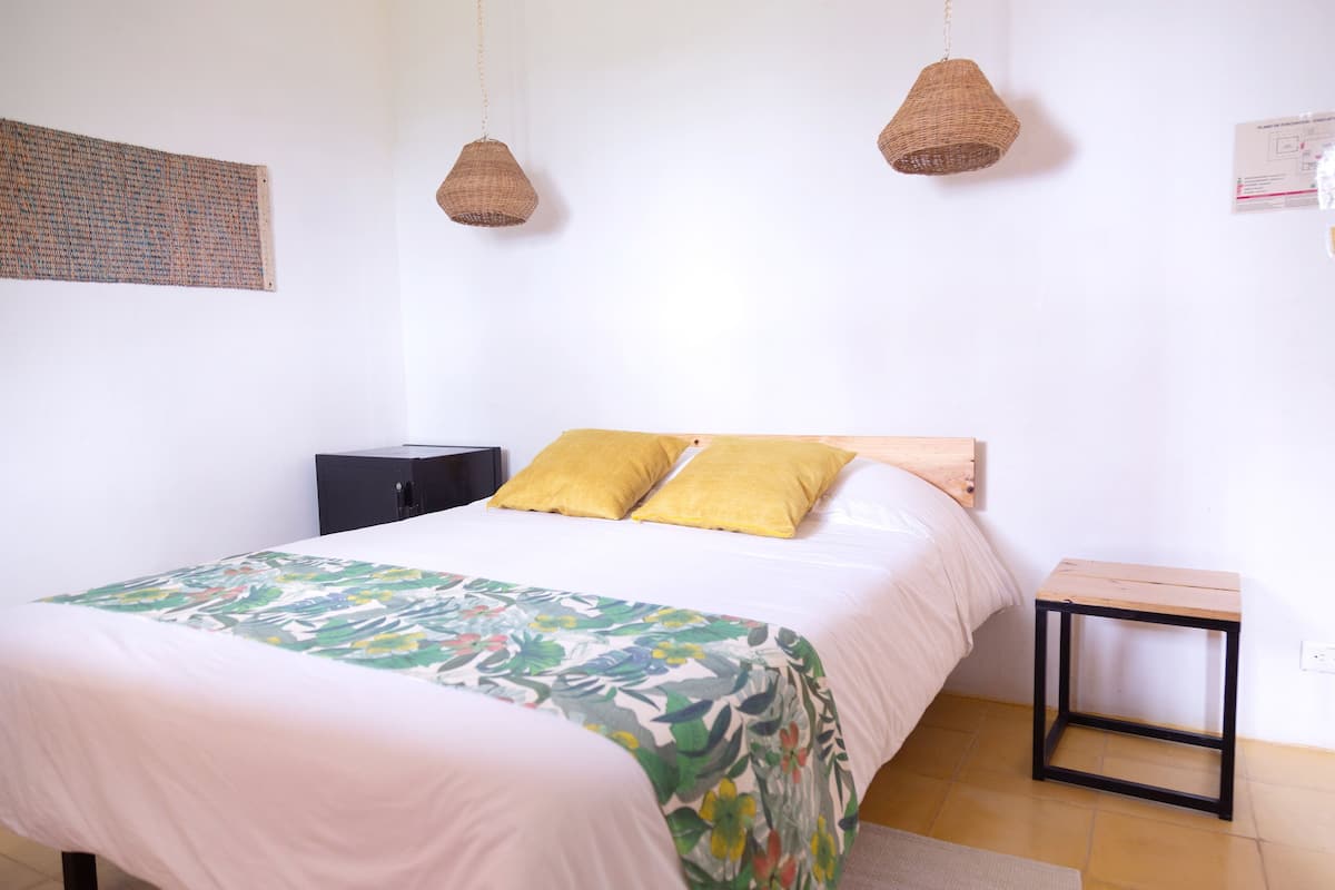 Ein Schlafzimmer mit einem Bett, zwei Hängelampen, einem kleinen Tisch und einem Wandbild.