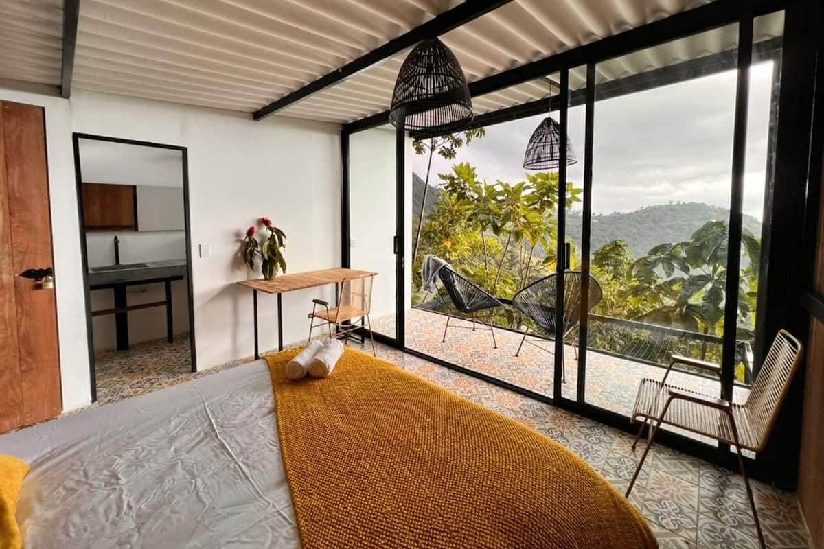 Ein Schlafzimmer mit einem großen Bett, Blick ins Freie und einem Balkon mit Sitzgelegenheiten.