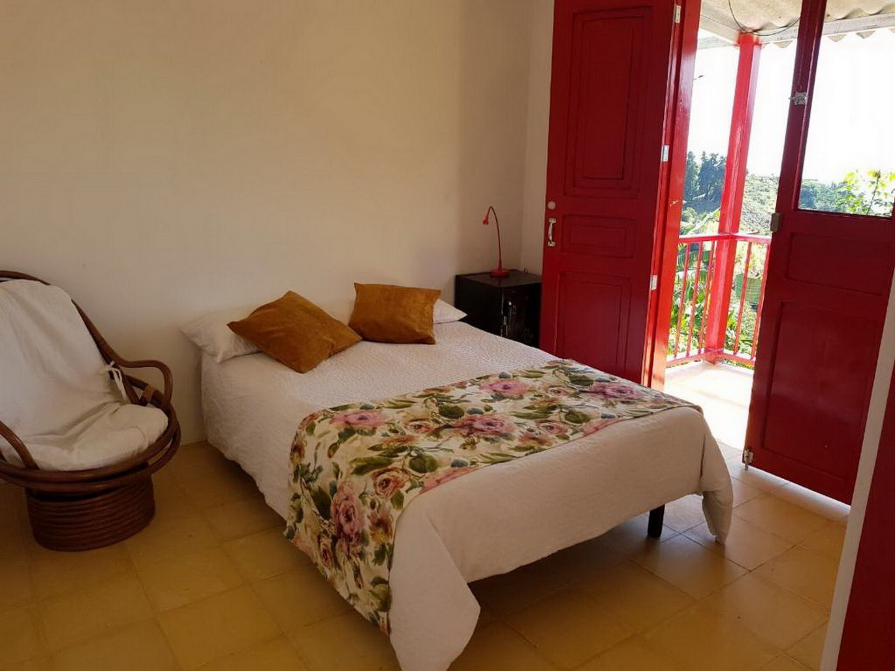 A bedroom with a bed, a chair, a nightstand, and a red door.