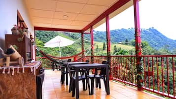 A covered outdoor area with tables and chairs, a hammock, and a view of a green landscape with hills.