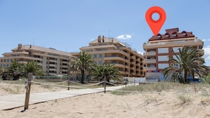 Un hôtel situé en bord de mer, doté de nombreux balcons, de palmiers et d’une plage de sable.