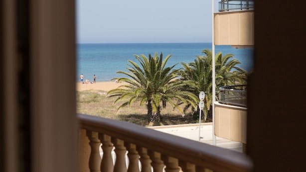 Un balcon avec vue sur la plage, les palmiers et un ciel dégagé.