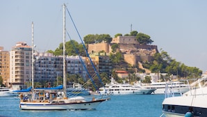 Un port de plaisance avec des bateaux amarrés, un château perché sur une colline et, au loin, des bâtiments modernes.