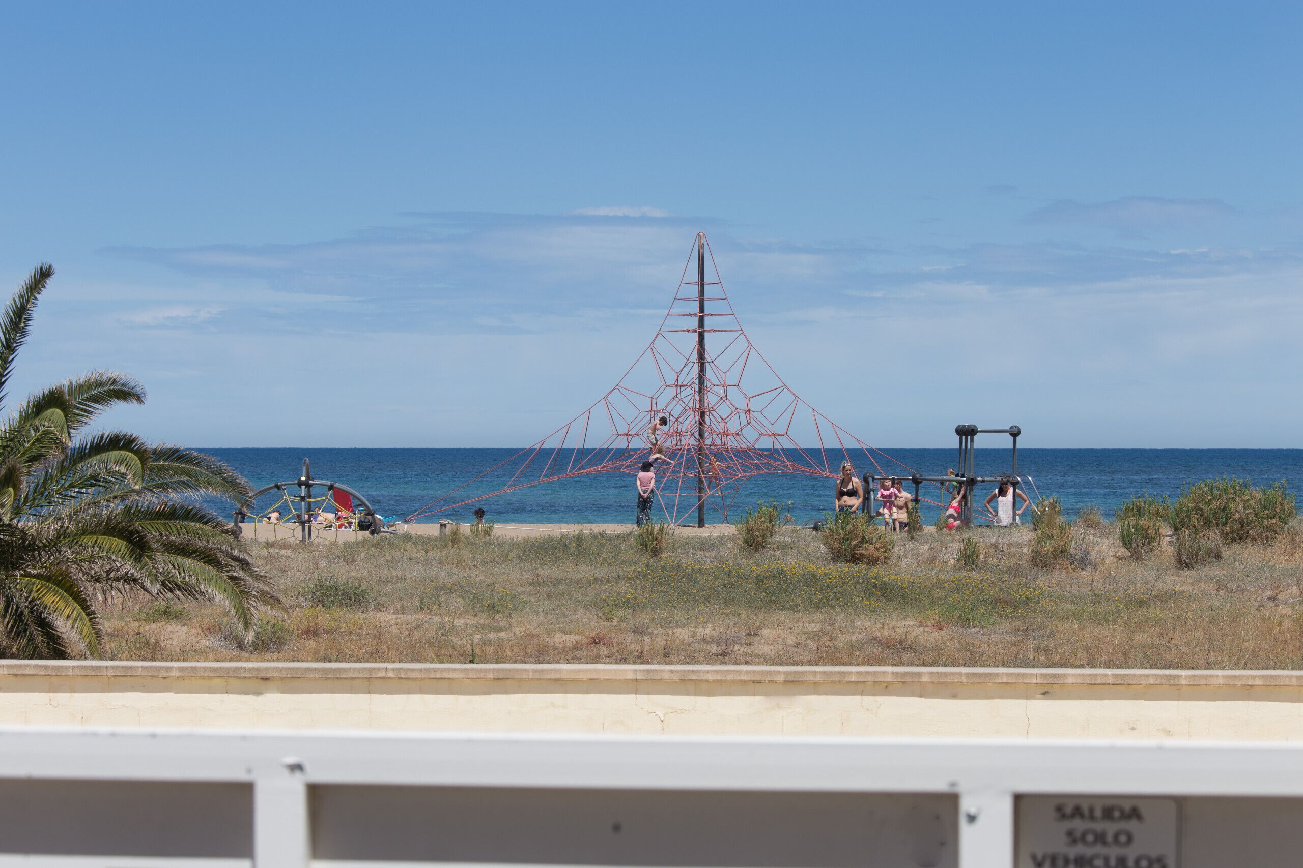 A beach with a large red metal structure, palm trees, and the sea in the background.