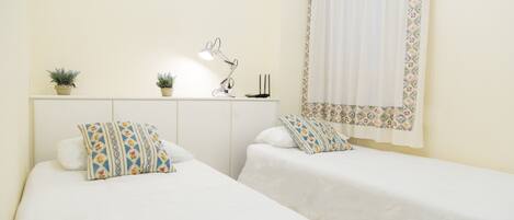 A bedroom with two beds, a desk with a lamp, and two potted plants.
