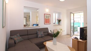 Un salon moderne avec un canapé d’angle marron, une table basse blanche, un téléviseur à écran plat posé sur un meuble en bois et un grand miroir accroché au mur.