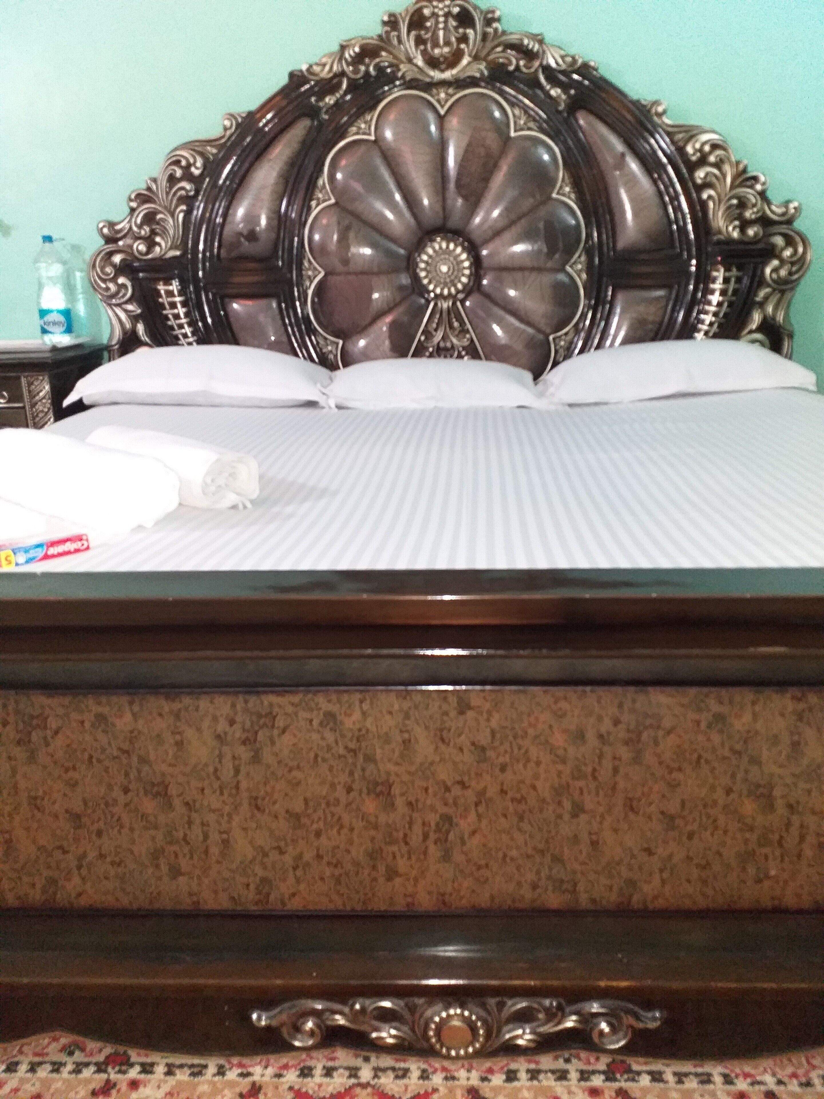 A bed with a floral headboard, white bedding, and a bottle of water on the nightstand.