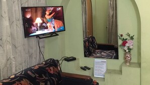 Sala de estar com televisão de tela plana na parede, um sofá, um espelho, um vaso com flores e uma mesinha com um controle remoto.