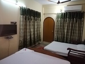 Una habitación con dos camas, un televisor montado en la pared, aire acondicionado y cortinas estampadas.
