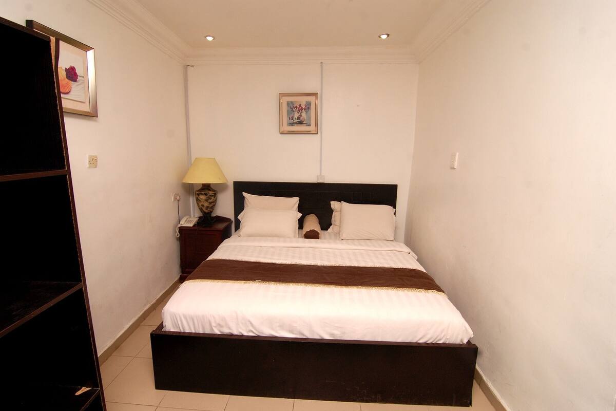 Un dormitorio con una cama grande, una mesita de noche con lámpara y un cuadro en la pared.
