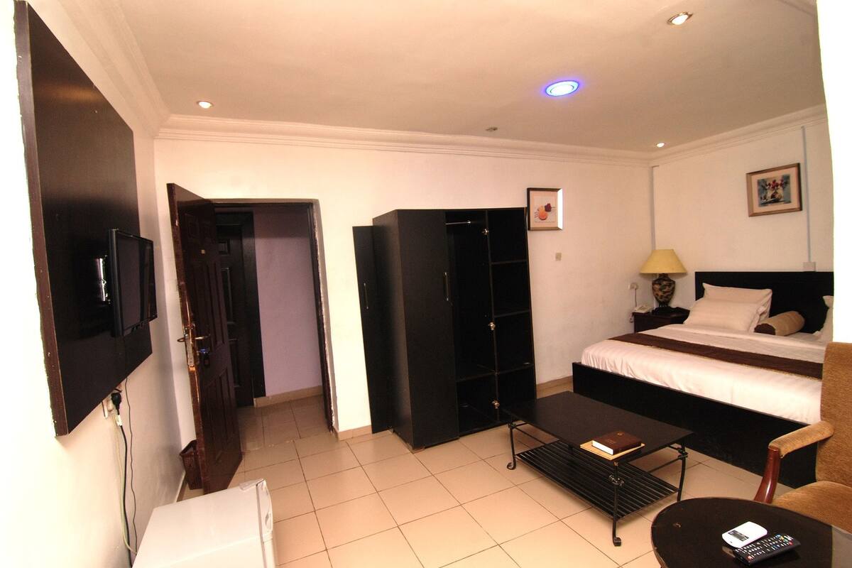 Habitación de hotel con cama, escritorio, silla, armario y televisor.